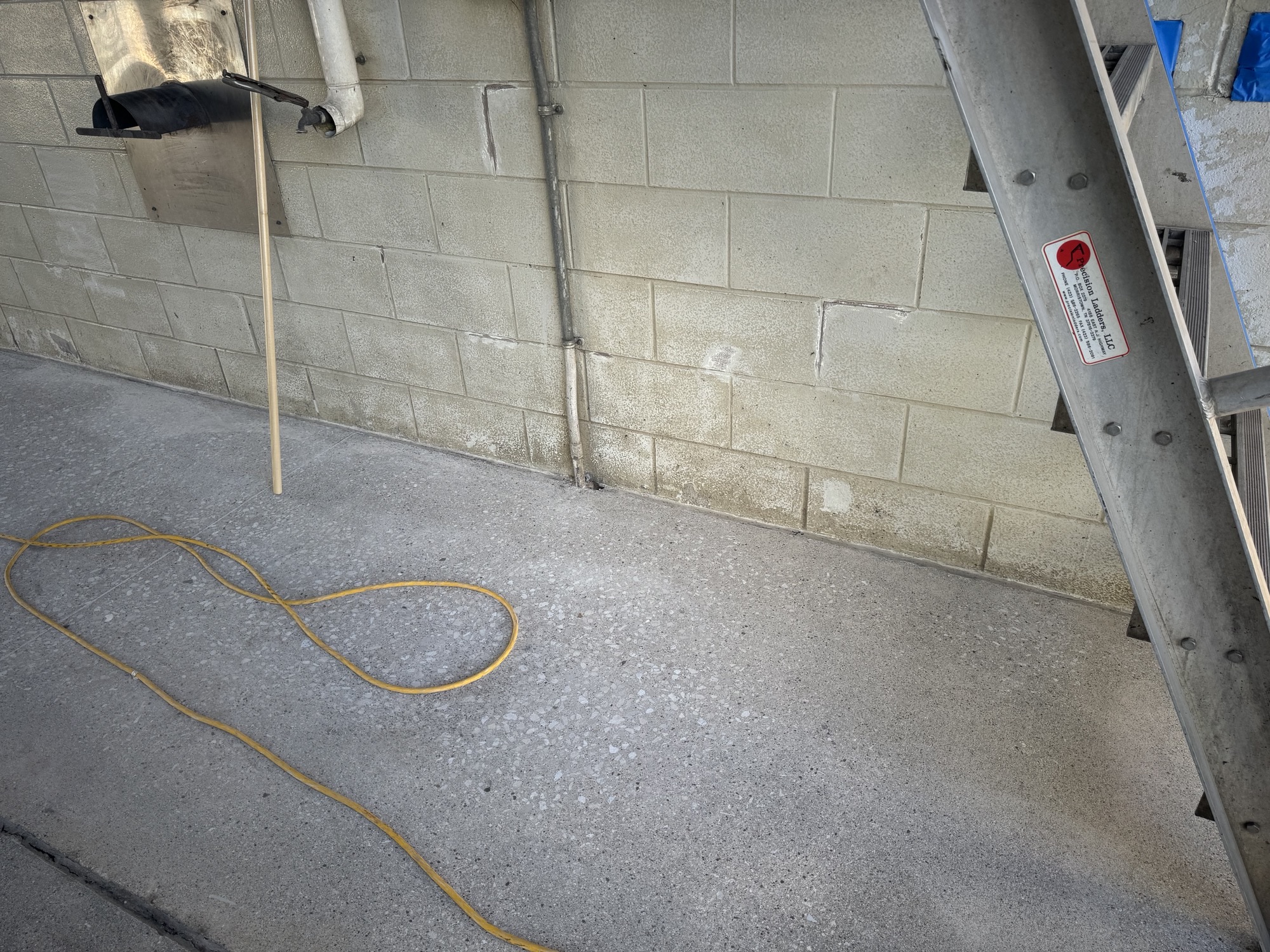 Damage survey: worn slab at the wall line with the surface paste gone and aggregate exposed — the profile the primer coat had to fill.