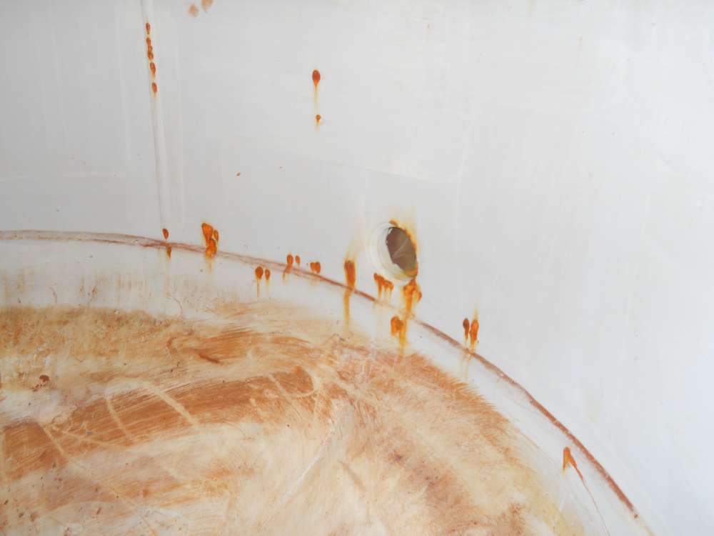 Before: rust bleeding through the failed lining along the floor-to-wall seam and around a fitting.