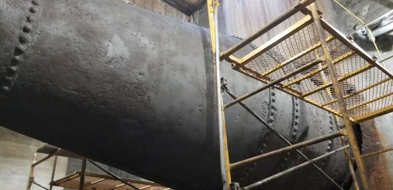 Before: corrosion along the shell and riveted lap joints, seen from beneath the pipe.