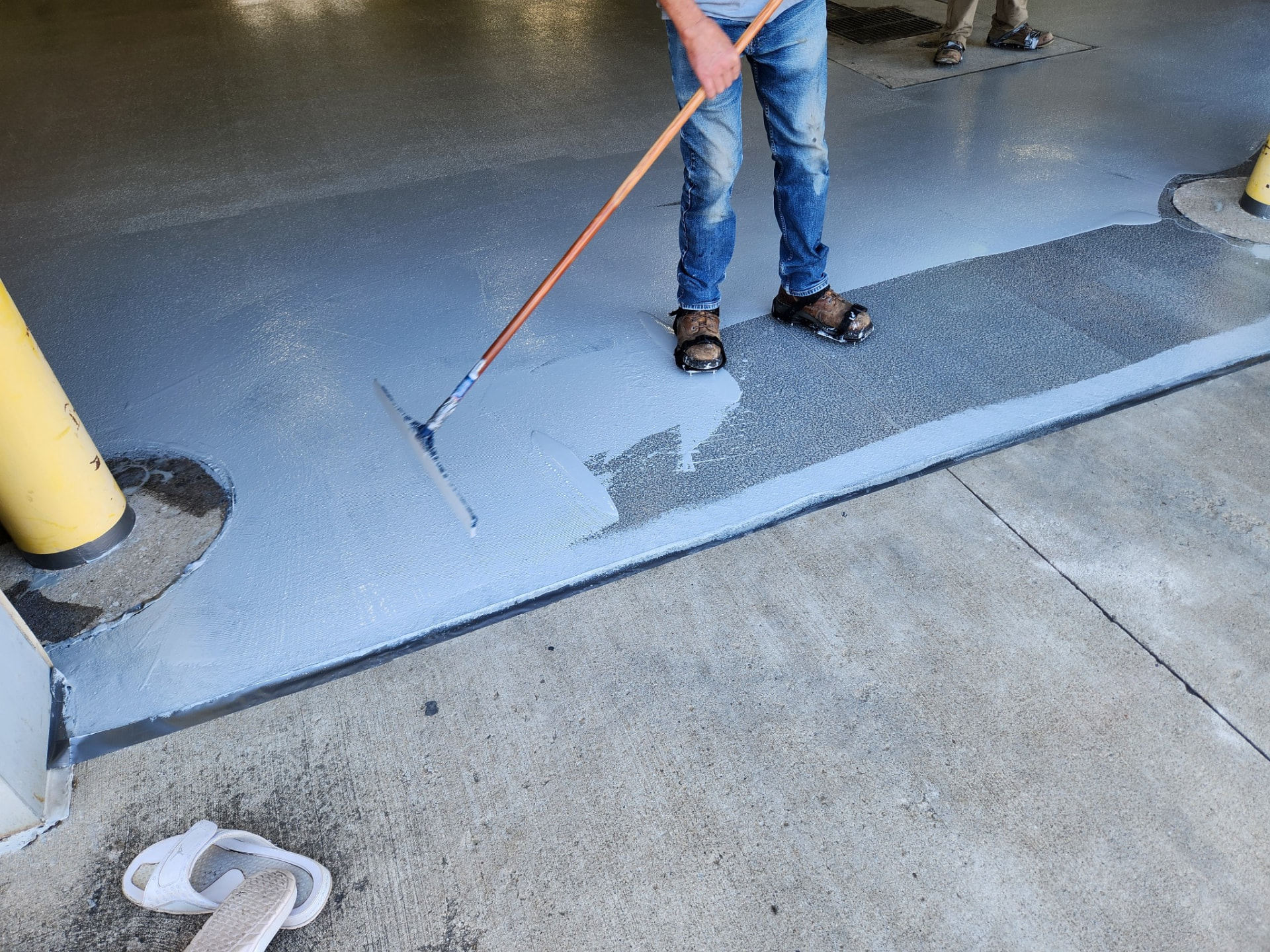 In progress — apron area: wet Belzona 5231 pulled out with a notched squeegee and back-rolled to hold an even 6-mil film up to the concrete edge.
