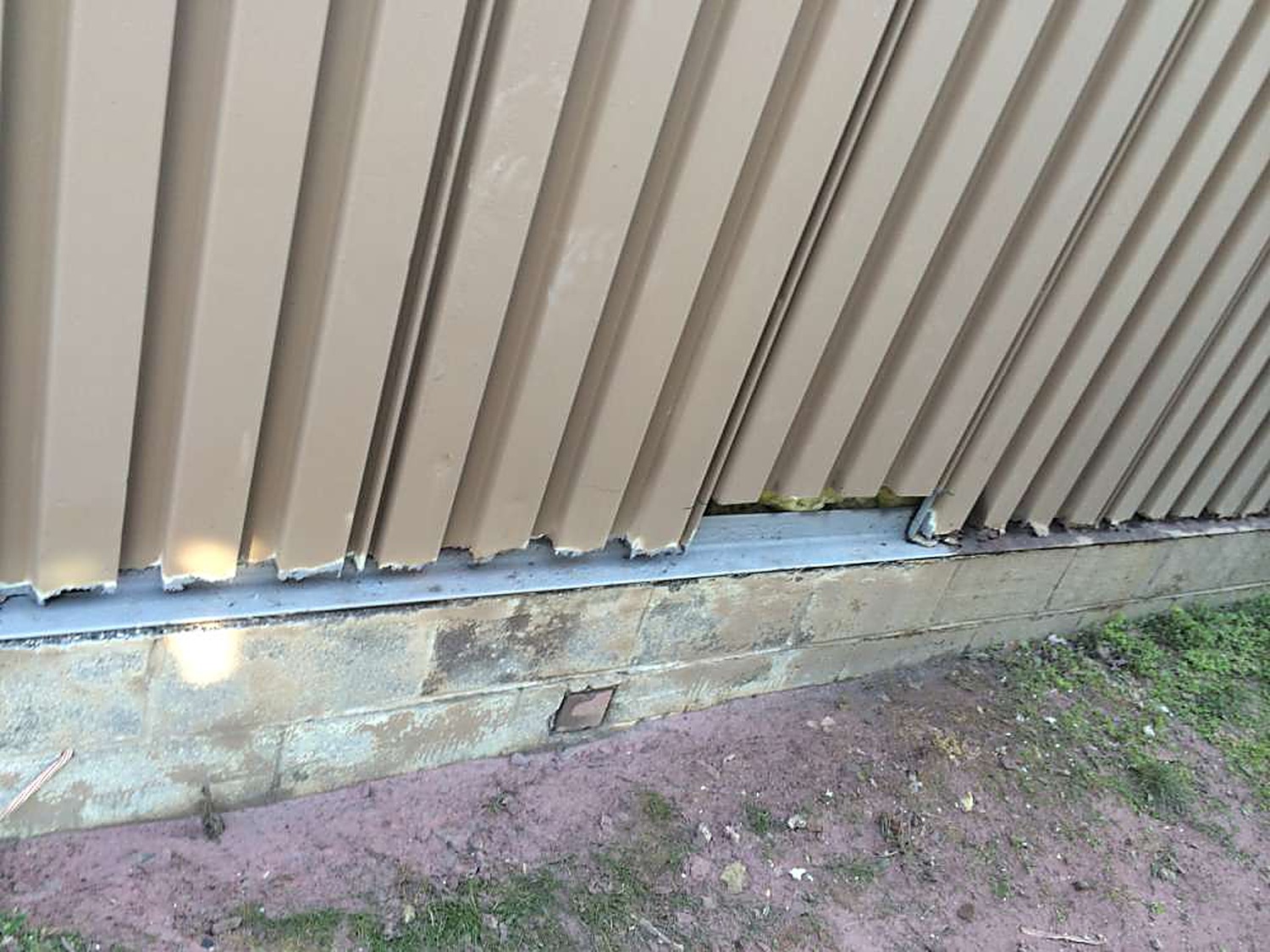 Exterior building wall with rotted-out siding panels and deteriorated concrete base