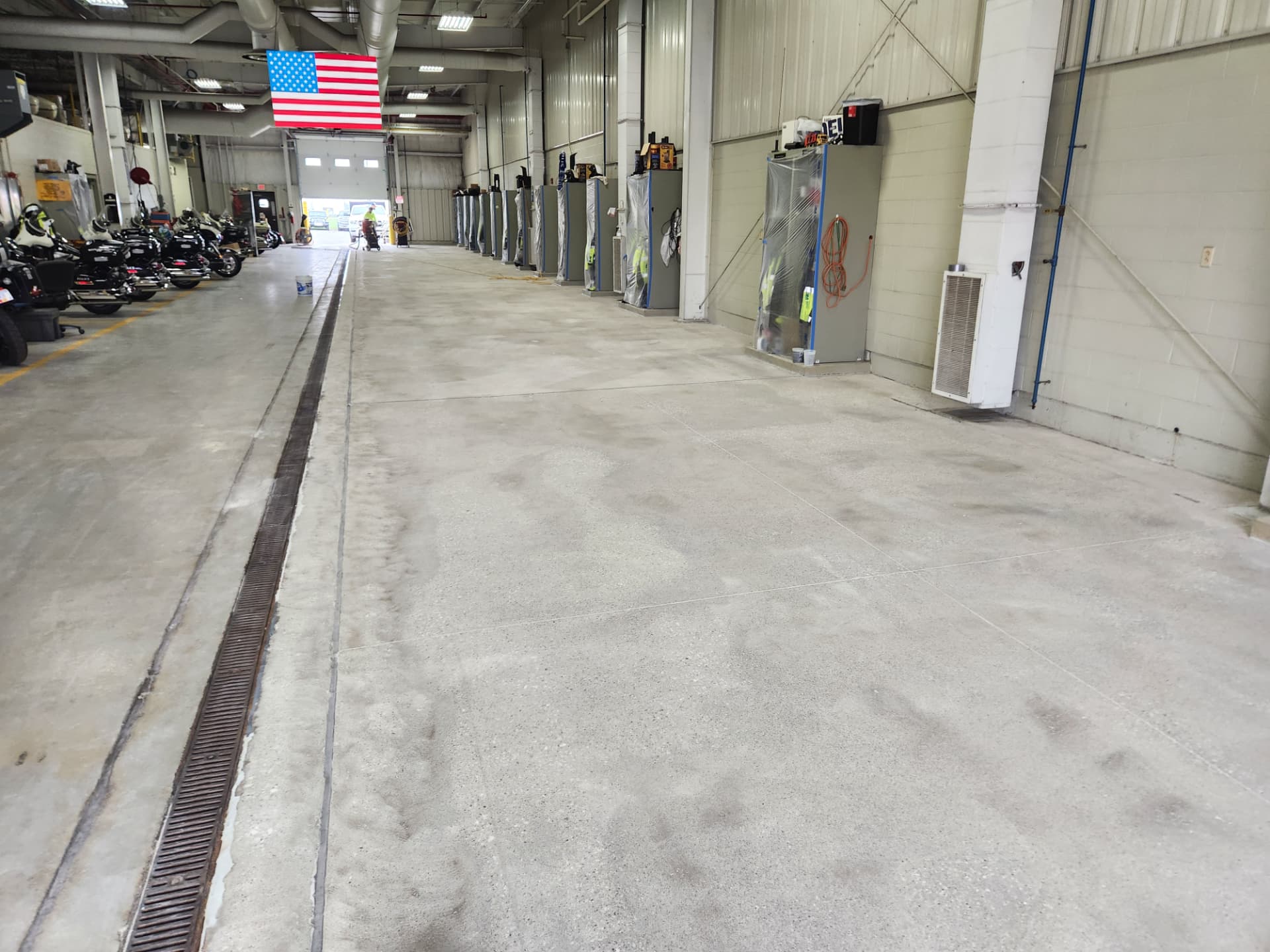 Before — motorcycle bay: patchy, discolored slab with tire tracking and a corroded trench drain edge.