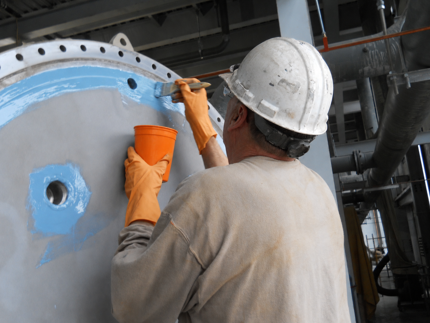 Technician brushing Belzona coating onto a vessel head with an orange mixing cup