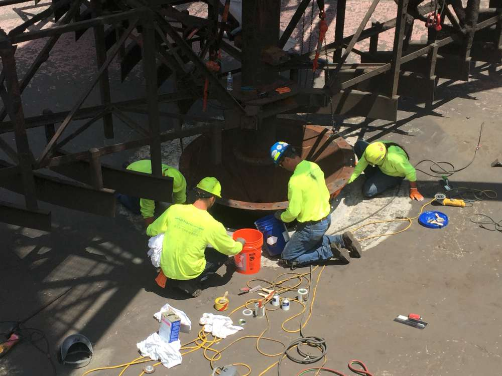 Technicians repairing the base of a large steel structure with Belzona materials